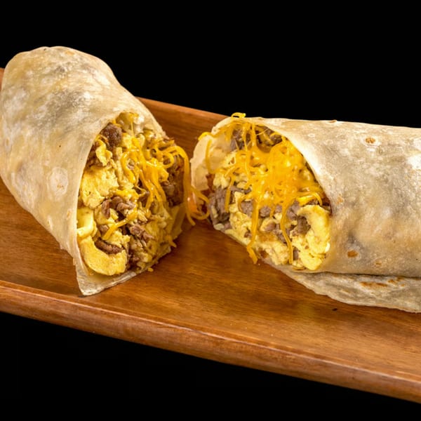 A large breakfast burrito, cut in half, revealing scrambled eggs, sausage, and melted cheese.