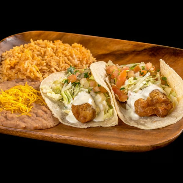 Two fish tacos with rice and refried beans on a wooden plate.