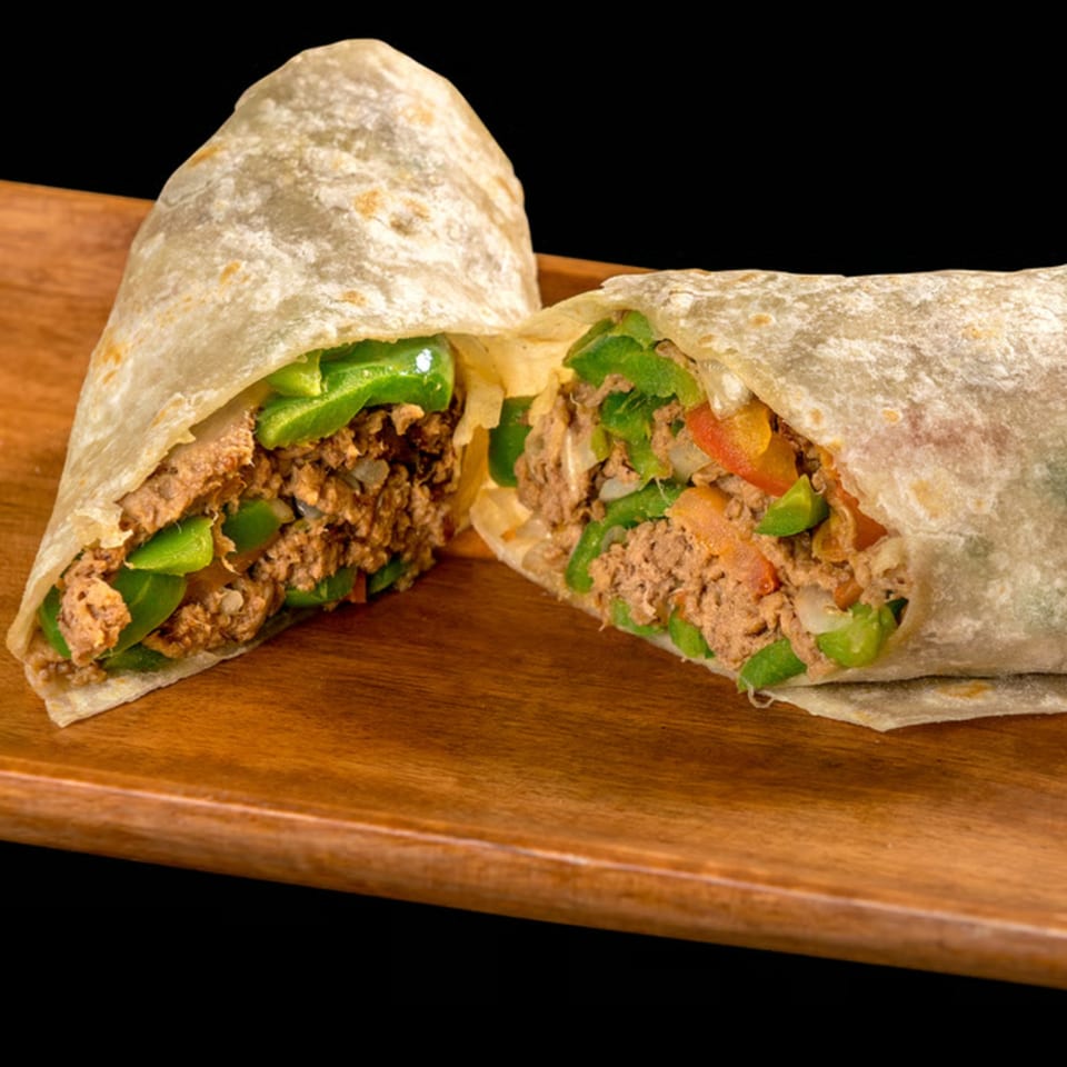 A large burrito, cut in half, revealing a filling of ground meat, green peppers, and onions.