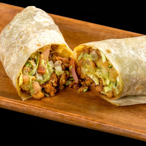 A large burrito, cut in half, revealing a filling of meat, guacamole, lettuce, and tomatoes.