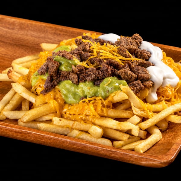 Loaded fries with melted cheese, ground beef, guacamole, and sour cream on a wooden tray.
